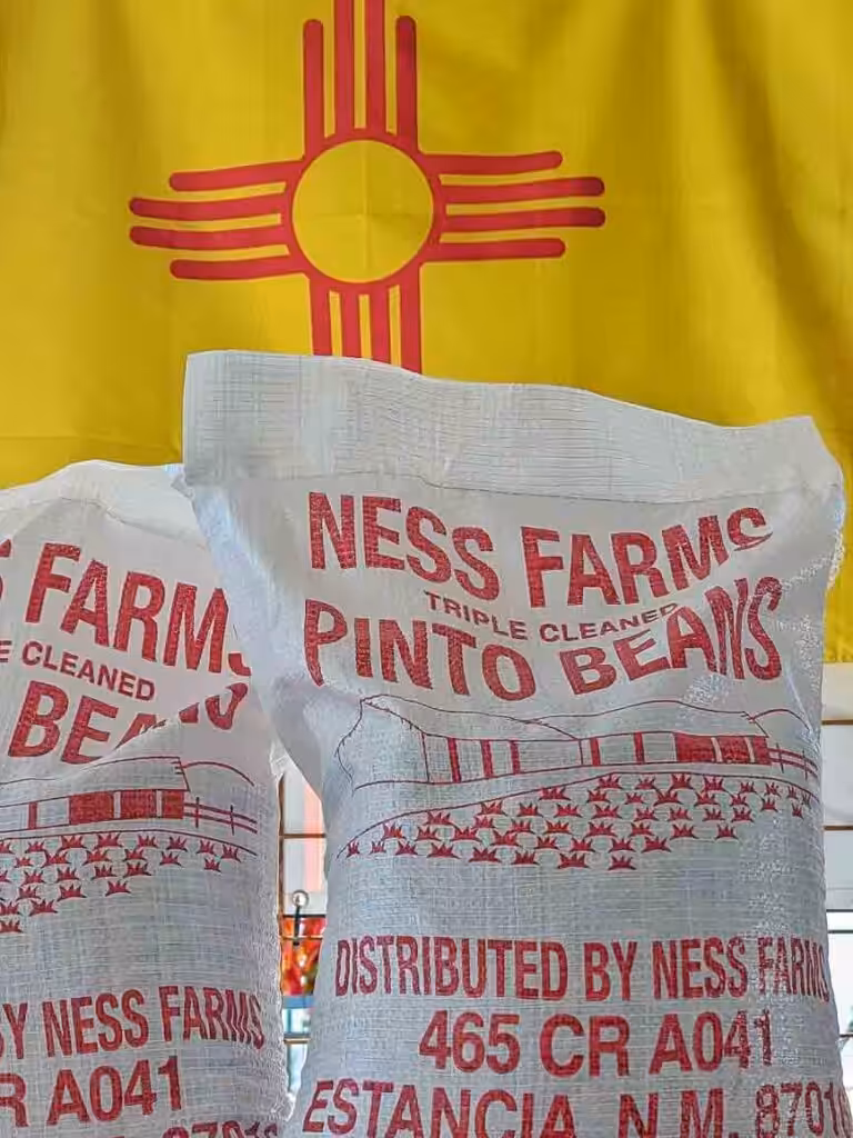 New Crop Estancia, New Mexico pinto bean sakcs in front of a New Mexican flag at Farmers Chile Market in Albuquerque