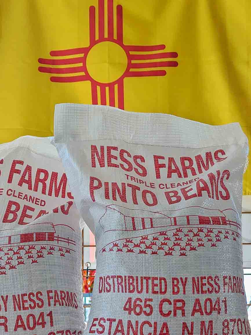 New Crop Estancia, New Mexico pinto bean sakcs in front of a New Mexican flag at Farmers Chile Market in Albuquerque