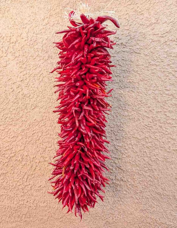 a 2 ft hatch pequin chile ristra in front of New Mexican adobe building