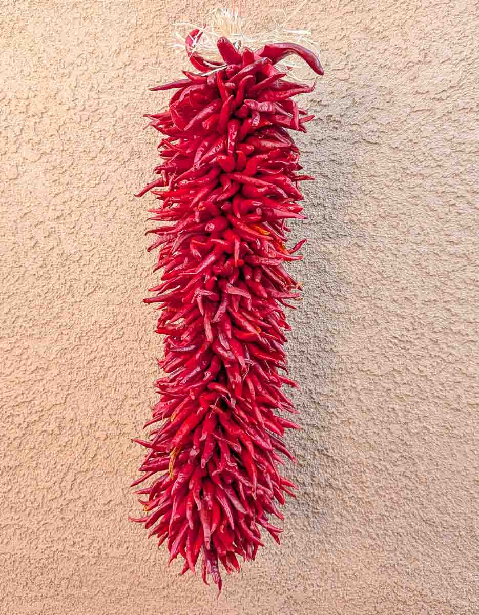 a 2 ft hatch pequin chile ristra in front of New Mexican adobe building