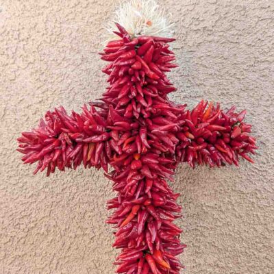 a special shapre Hatch pequin chile ristra cross in front of a New Mexican stucco building