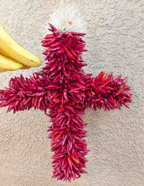 a hatch chile pequin ristra wreath with a banana next to it in front of adobe