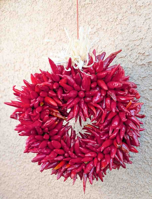 a small Hatch pequin chile ristra wreath in front of New Mexican stucco building