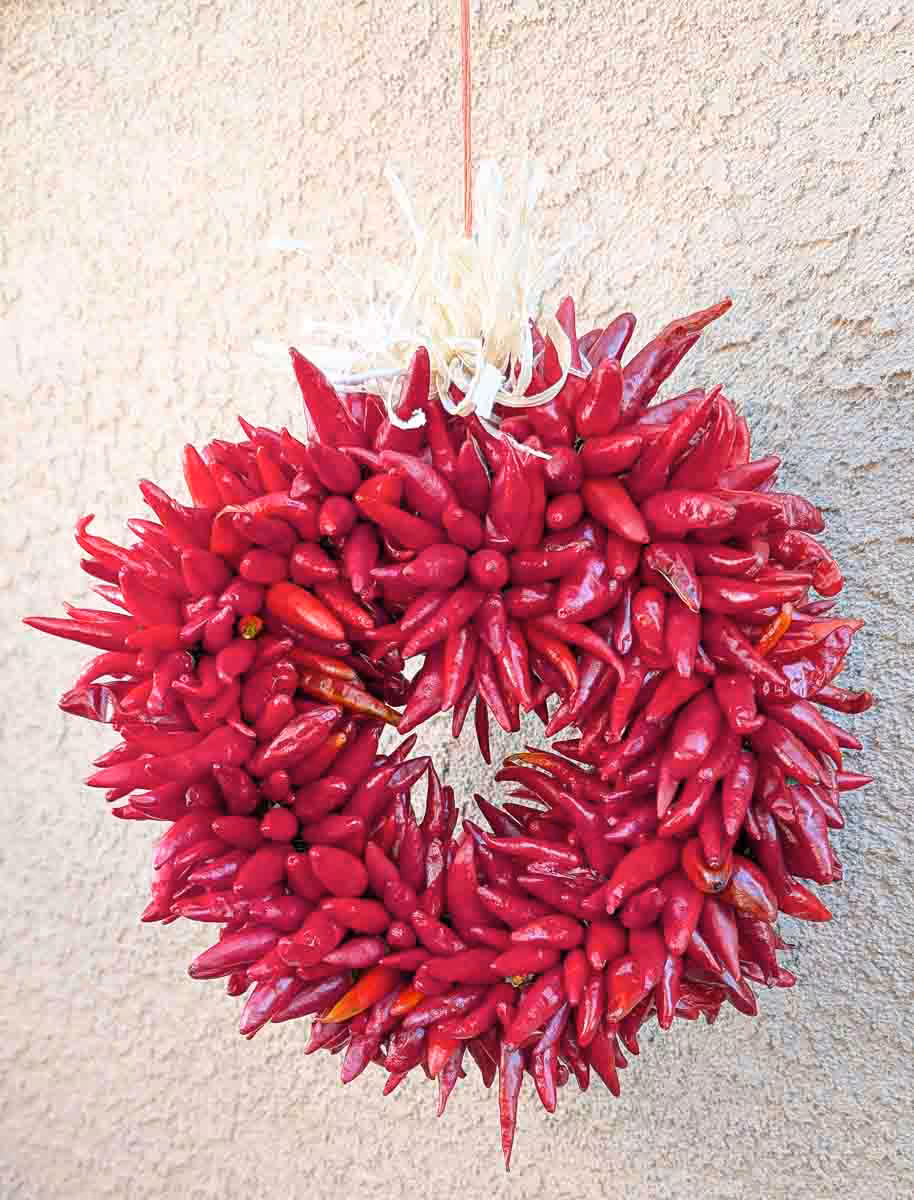 a small Hatch pequin chile ristra wreath in front of New Mexican stucco building